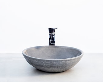 May include: A round, gray stone vessel sink with a black faucet.