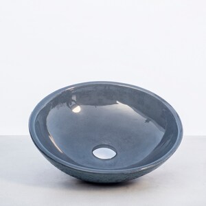 May include: A gray ceramic vessel sink with a smooth, rounded interior and a small drain hole in the center.