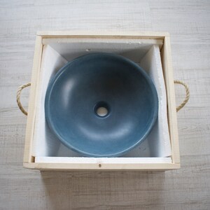 May include: A blue ceramic sink in a wooden box with foam padding. The sink has a round shape with a small drain hole in the center.