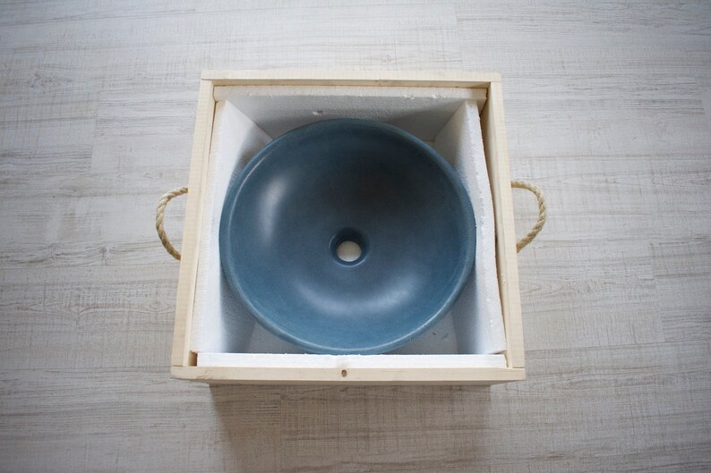 May include: A blue ceramic sink in a wooden box with foam padding. The sink has a round shape with a small drain hole in the center.
