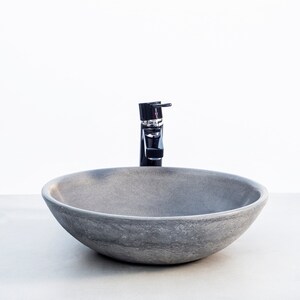 May include: A round, gray stone vessel sink with a black faucet. The sink is on a white countertop.
