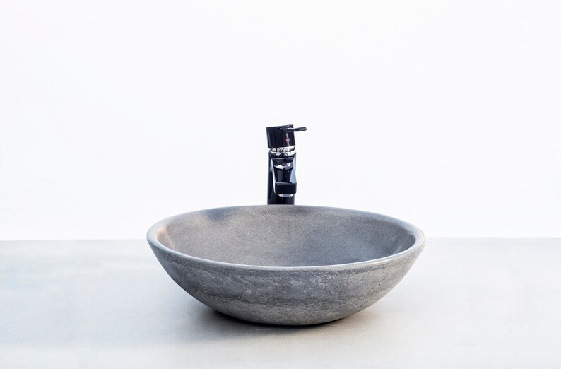 May include: A round, gray stone vessel sink with a black faucet. The sink is on a white countertop.