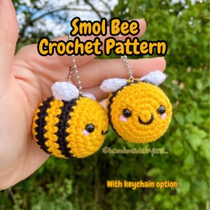 Könnte beinhalten: Zwei handgefertigte Häkel-Bienen-Schlüsselanhänger. Die Bienen sind gelb mit schwarzen Streifen und weißen Flügeln. Jede Biene hat ein lächelndes Gesicht mit rosa Wangen und schwarzen Augen. Der Text "Smol Bee Crochet Pattern" steht oben und "With keychain option" unten.