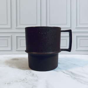 May include: A dark brown mug with a textured, matte finish on the upper portion and a smooth, solid base. The mug features a distinct horizontal ridge separating the two sections and a square-shaped handle extending from the right side.