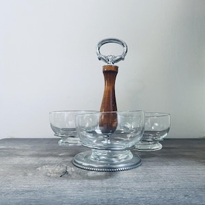 May include: A vintage serving piece with three clear glass bowls and a wooden handle. The handle is topped with a decorative silver-toned metal ring. The bowls sit on a silver-toned metal base, perfect for serving desserts or appetizers.