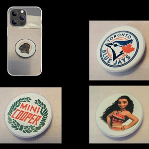 Op de afbeelding: Vier verschillende telefoon popsocket-ontwerpen. De eerste is een zwart-wit afbeelding van Darth Vader. De tweede is een blauw en wit Toronto Blue Jays logo. De derde is een groen en wit Mini Cooper logo. De vierde is een kleuren afbeelding van Moana uit de Disney film Moana.