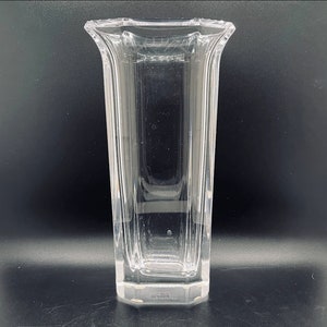 May include: A clear glass vase with a square base and a rectangular body. The vase has a slightly flared opening.