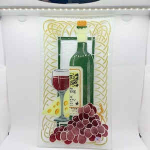 May include: A rectangular glass serving tray with a wine theme. The image features a green wine bottle, a glass of red wine, a wedge of cheese, and a bunch of grapes. The background has a gold Celtic knot design.