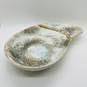 May include: A white ceramic serving dish with a speckled brown and blue glaze. The dish has a gold trim and a gold chain design on the side.