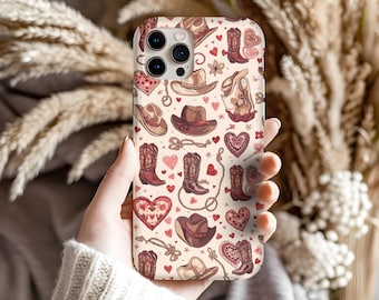 May include: A phone case featuring a repeating pattern of cowboy hats, boots, hearts, and rope on a cream background. The design uses shades of brown, red, and pink. The case is held in a person's hand.