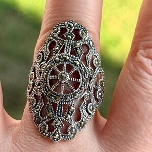 Puede incluir: Un anillo de plata ornamentado con un dise&ntilde;o de filigrana detallado. El anillo presenta un patr&oacute;n central en forma de rueda y est&aacute; adornado con peque&ntilde;os acentos brillantes. Este anillo es una pieza llamativa, perfecta para a&ntilde;adir elegancia.