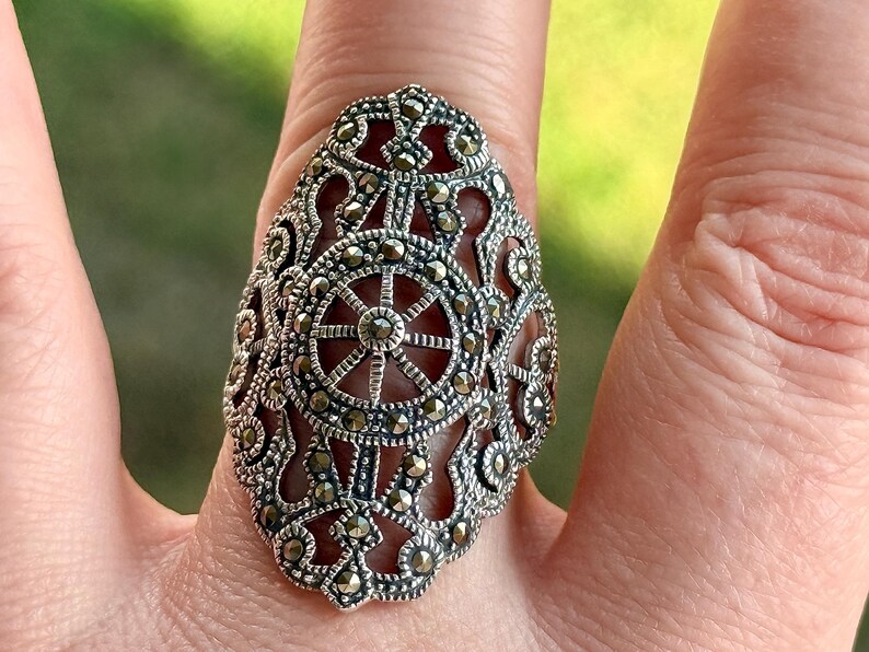 Puede incluir: Un anillo de plata ornamentado con un dise&ntilde;o de filigrana detallado. El anillo presenta un patr&oacute;n central en forma de rueda y est&aacute; adornado con peque&ntilde;os acentos brillantes. Este anillo es una pieza llamativa, perfecta para a&ntilde;adir elegancia.