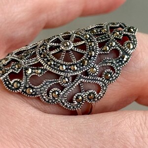 Puede incluir: Anillo plateado ornamentado con un dise&ntilde;o de filigrana. El anillo presenta un patr&oacute;n circular central y est&aacute; adornado con peque&ntilde;as piedras brillantes. Los intrincados detalles y los acentos oscuros crean una est&eacute;tica vintage.