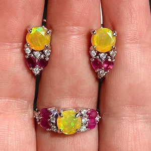 May include: A jewelry set featuring a ring and matching earrings. The ring and earrings have a silver setting with a large yellow gemstone, surrounded by smaller red and clear gemstones. The earrings are studs.