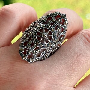 Puede incluir: Un anillo ovalado de plata con intrincados detalles de filigrana y marcasita. El anillo presenta un dise&ntilde;o central que se asemeja a una rueda o un sol, rodeado de patrones ornamentados. El anillo se lleva en un dedo.
