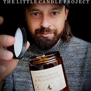 May include: A brown glass candle jar with a white label that reads "The Amber Collection Sandalwood & Blackpepper The Little Candle Project Aberdeen, Scotland".