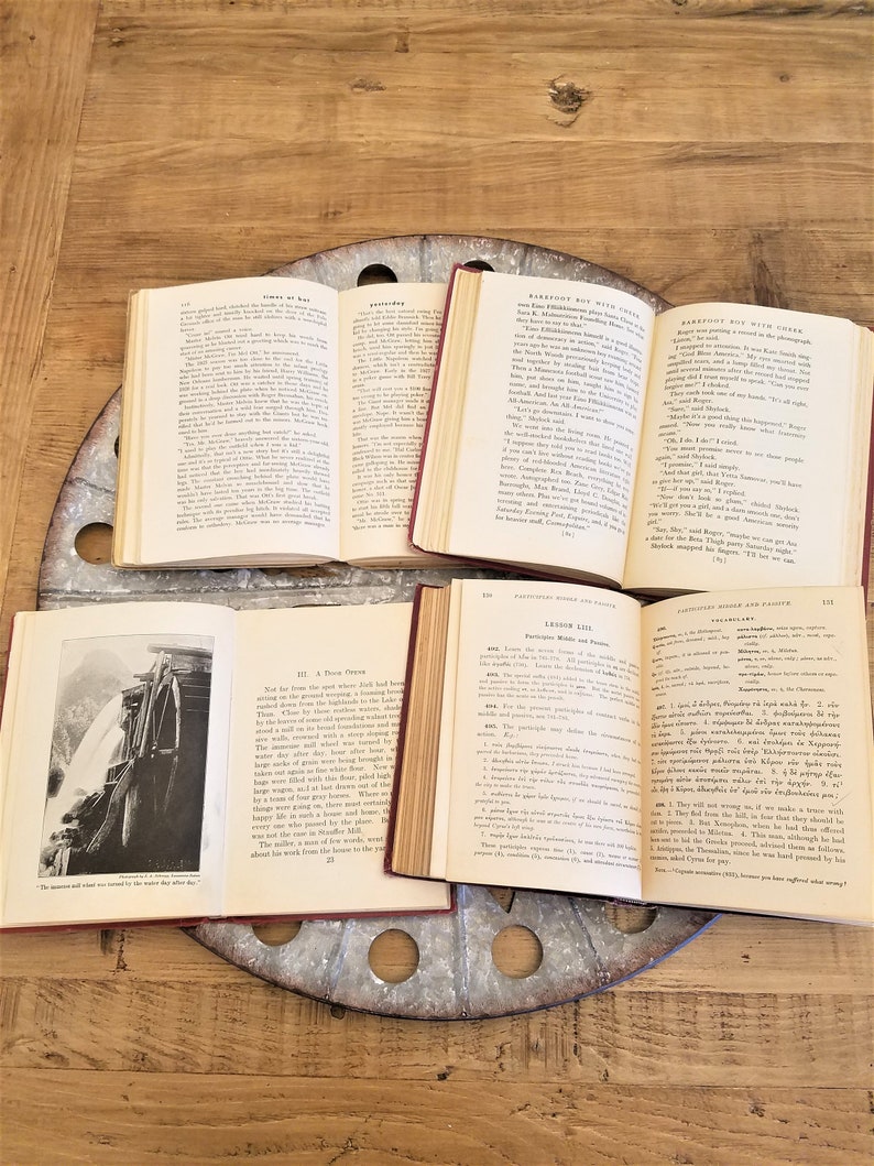 May include: Four open books with different titles and text. The books are on a wooden table with a metal spool in the center. The books are all open to different pages and show different text. The books are all in good condition and have no visible damage.