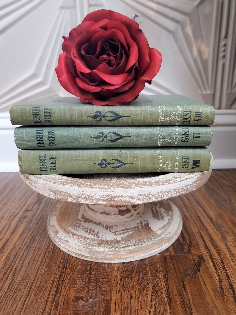 Pu&ograve; includere: Una pila di tre libri in copertina rigida verde con scritte dorate sui dorsi. I libri sono intitolati "Hebbel Briefe" e sono impilati su un piedistallo di legno bianco. Una rosa rossa &egrave; appoggiata sopra i libri.