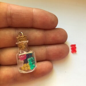 May include: A small glass bottle charm with a cork stopper filled with colorful gummy bears. The bottle has a gold loop for hanging. A single red gummy bear is shown next to the bottle.