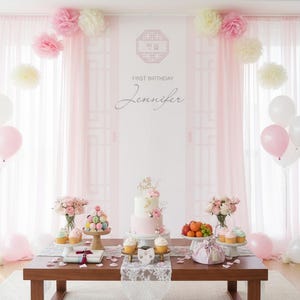 May include: A first birthday party setup with a cake, cupcakes, and macarons on a wooden table. Pink and white balloons, flowers, and paper decorations adorn the room. The backdrop features the text "First Birthday Jennifer."