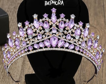 May include: A gold crown with purple and clear rhinestones. The crown is on a black stand with the text "BEPHORA" on it.