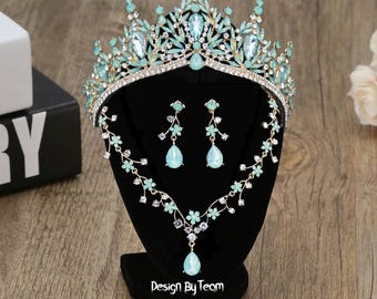 May include: A light blue and gold bridal crown, necklace, and earrings set. The crown is adorned with rhinestones and faux pearls. The necklace and earrings feature a teardrop design with a floral motif.