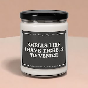 May include: A white candle jar with a black lid and label. The label says "Smells Like I Have Tickets To Venice".