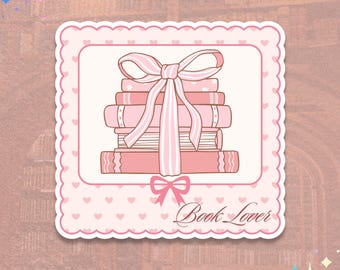 May include: A pink sticker with a stack of books tied with a pink ribbon. The sticker has a scalloped edge and a heart pattern. The words "Book Lover" are written in cursive.