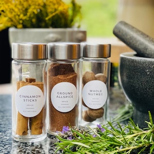 May include: Three glass jars with silver lids containing cinnamon sticks, ground allspice, and whole nutmeg. The jars are labeled with the spice name and "All Natural".