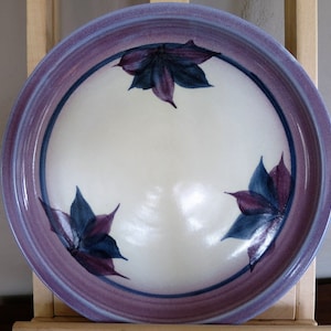 May include: A white ceramic bowl with a purple rim and three stylized purple and blue leaf designs.