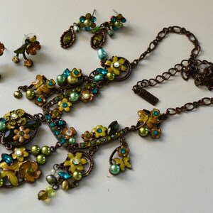May include: A floral jewelry set featuring a necklace and two pairs of earrings. The set includes a necklace with yellow and green flower accents, teal and green beads, and a matching pair of drop earrings and stud earrings.