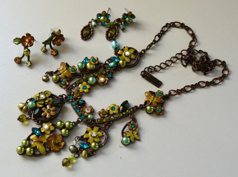 May include: A floral jewelry set featuring a necklace and two pairs of earrings. The set includes a necklace with yellow and green flower accents, teal and green beads, and a matching pair of drop earrings and stud earrings.
