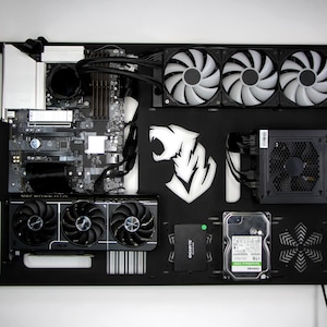 Op de afbeelding: Een zwarte computerkast met diverse componenten, waaronder een moederbord, grafische kaart, ventilatoren en voeding. Een wit tijgerlogo is zichtbaar. De componenten zijn gerangschikt op een zwart oppervlak.