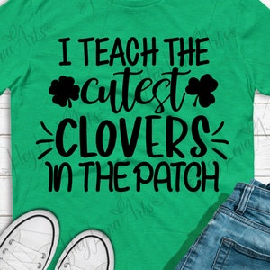 Może przedstawiać: Zielona koszulka z napisem "I teach the cutest clovers in the patch" czarnymi literami. Tekst jest otoczony dwoma wzorami koniczyny.