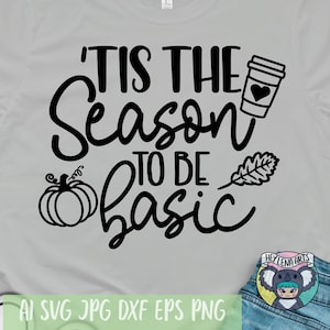 May include: A gray t-shirt with the text "'Tis the season to be basic" in black. The design includes a pumpkin, a coffee cup with a heart, and a leaf. The text "Hey Lena Arts" is in a circle with a koala bear graphic.