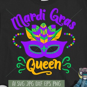 May include: A black t-shirt with the text "Mardi Gras Queen" in purple, green, and yellow. The design includes a purple mask with green and yellow beads, and a green and yellow feather design.