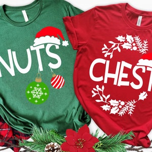 May include: Two Christmas themed t-shirts, one green with the word "NUTS" and a Santa hat ornament, and one red with the word "CHEST" and a wreath of holly.