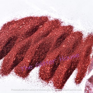 May include: A close-up of a pile of red glitter. The glitter is in a clear plastic bag with the text "The Glitter House" printed on it.