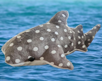 May include: A gray and white plush whale shark with white spots. The plush toy is lying on its side in the water.