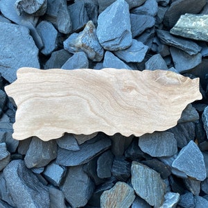 May include: A wooden cutout of the island of Puerto Rico, resting on a bed of dark gray slate stones.