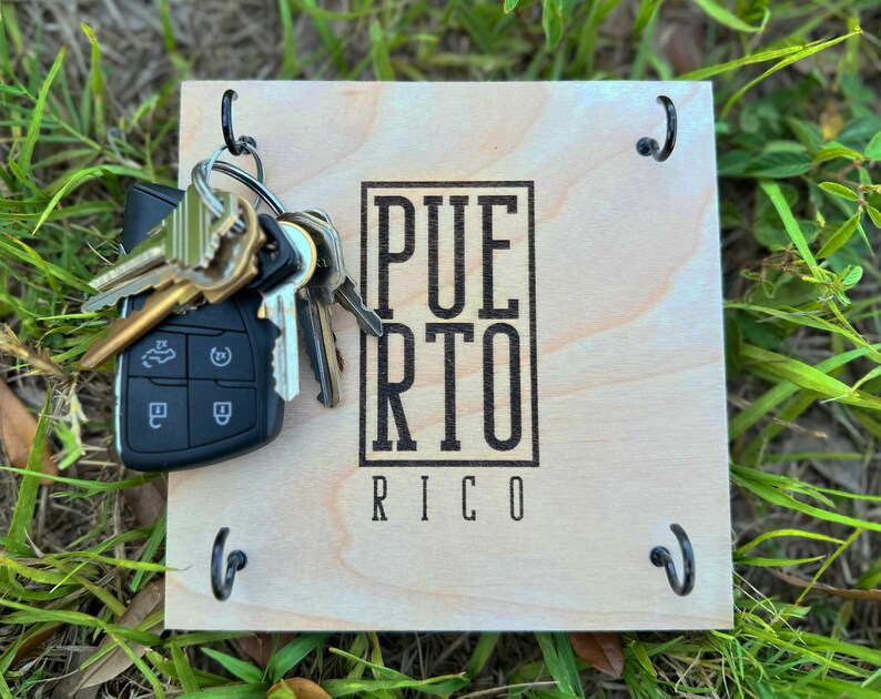 K&ouml;nnte beinhalten: Ein h&ouml;lzerner Schl&uuml;sselhalter mit dem Text "PUERTO RICO" in einem schwarzen rechteckigen Rahmen. Der Schl&uuml;sselhalter hat vier schwarze Haken und einen Satz Schl&uuml;ssel, einschlie&szlig;lich eines Autoschl&uuml;ssels.