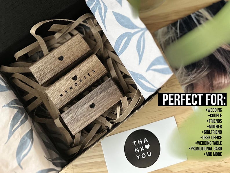 Puede incluir: Tres bloques de madera apilados uno encima del otro en una caja. Los bloques son marrones y tienen un coraz&oacute;n y la palabra "MEMORIES" grabada en ellos. La caja est&aacute; forrada con papel marr&oacute;n y tiene un papel estampado blanco y azul en el lateral. Una tarjeta con el texto "THANK YOU" es visible en la esquina inferior derecha de la imagen.