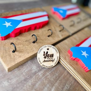 K&ouml;nnte beinhalten: Schl&uuml;sselhalter aus Holz mit drei Haken, mit einem roten, wei&szlig;en und blauen Ausschnitt der puerto-ricanischen Flagge. Der Schl&uuml;sselhalter hat auch einen kleinen Holzkreis mit dem Text "You are amazing!" und "Thanks for your support!"