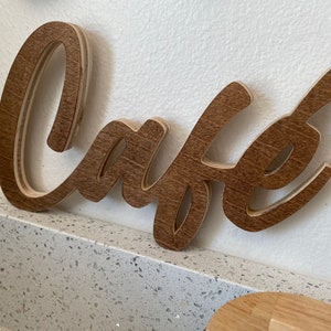 May include: A wooden sign with the word "Cafe" written in a cursive font. The sign is brown and has a natural wood grain.