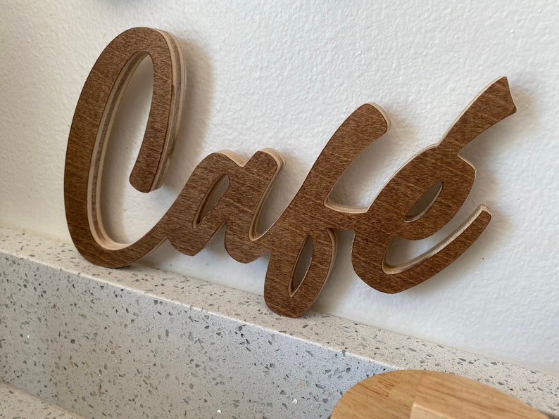 May include: A wooden sign with the word "Cafe" written in a cursive font. The sign is brown and has a natural wood grain.