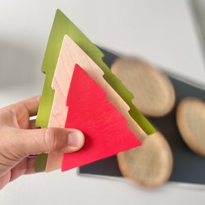 May include: Three wooden Christmas tree ornaments stacked on top of each other. The bottom ornament is green, the middle ornament is beige, and the top ornament is red.