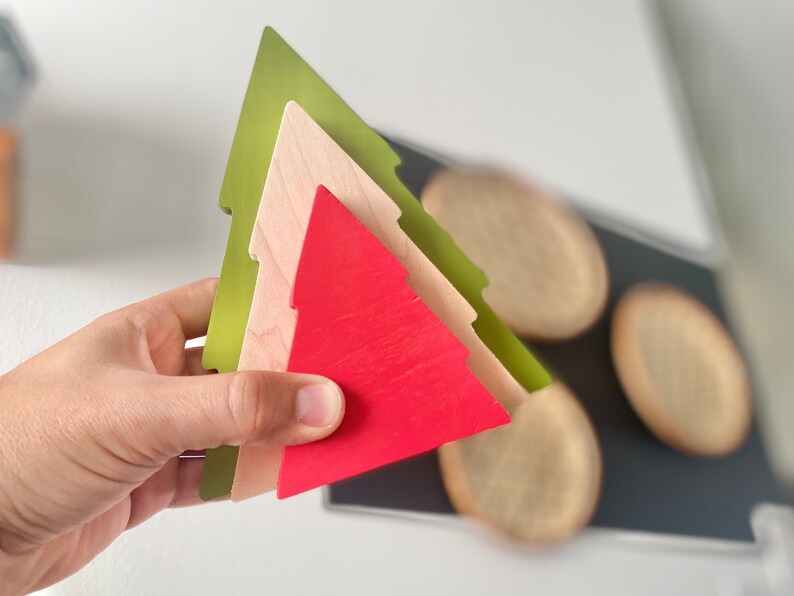 May include: Three wooden Christmas tree ornaments stacked on top of each other. The bottom ornament is green, the middle ornament is beige, and the top ornament is red.