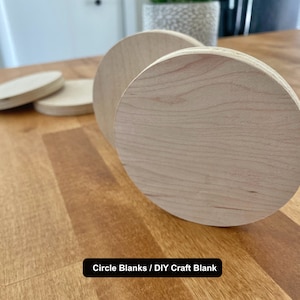 May include: Four unfinished wooden circle blanks, ideal for DIY crafts. The blanks are light brown and have a smooth surface. The text "Circle Blanks / DIY Craft Blank" is visible at the bottom of the image.
