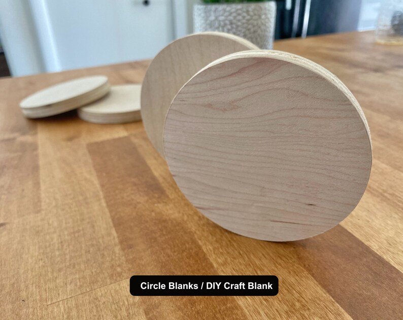 May include: Four unfinished wooden circle blanks, ideal for DIY crafts. The blanks are light brown and have a smooth surface. The text "Circle Blanks / DIY Craft Blank" is visible at the bottom of the image.