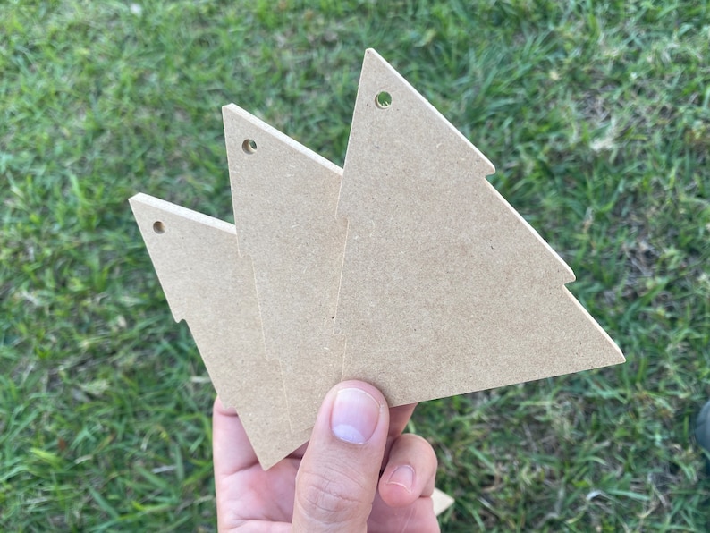 May include: Three unfinished wooden Christmas tree decorations with a hole at the top for hanging.